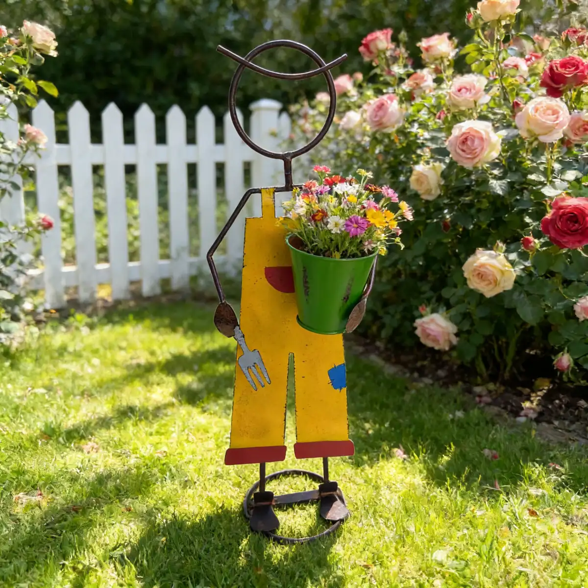 Whimsical metal gardener figurine by a white picket fence